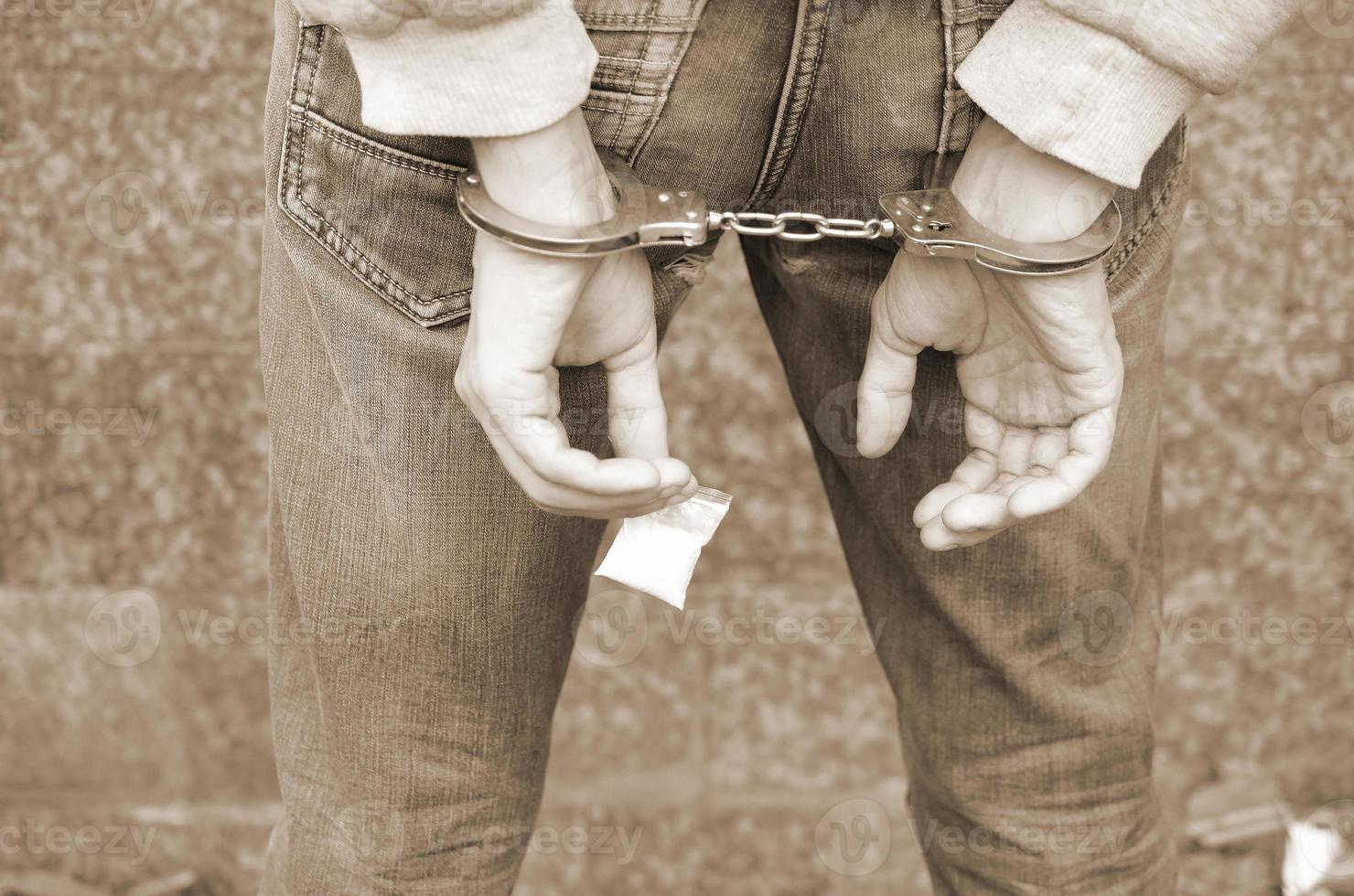 arrestato droga commerciante nel polizia manette con piccolo eroina droga pacchetto su buio parete sfondo foto