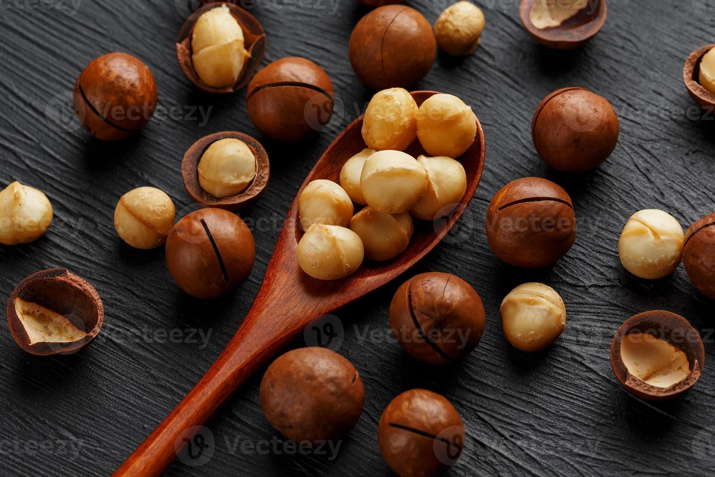 sgusciate macadamia Noce e pelato macadamia Noce su un' nero strutturale sfondo nel un' di legno cucchiaio foto