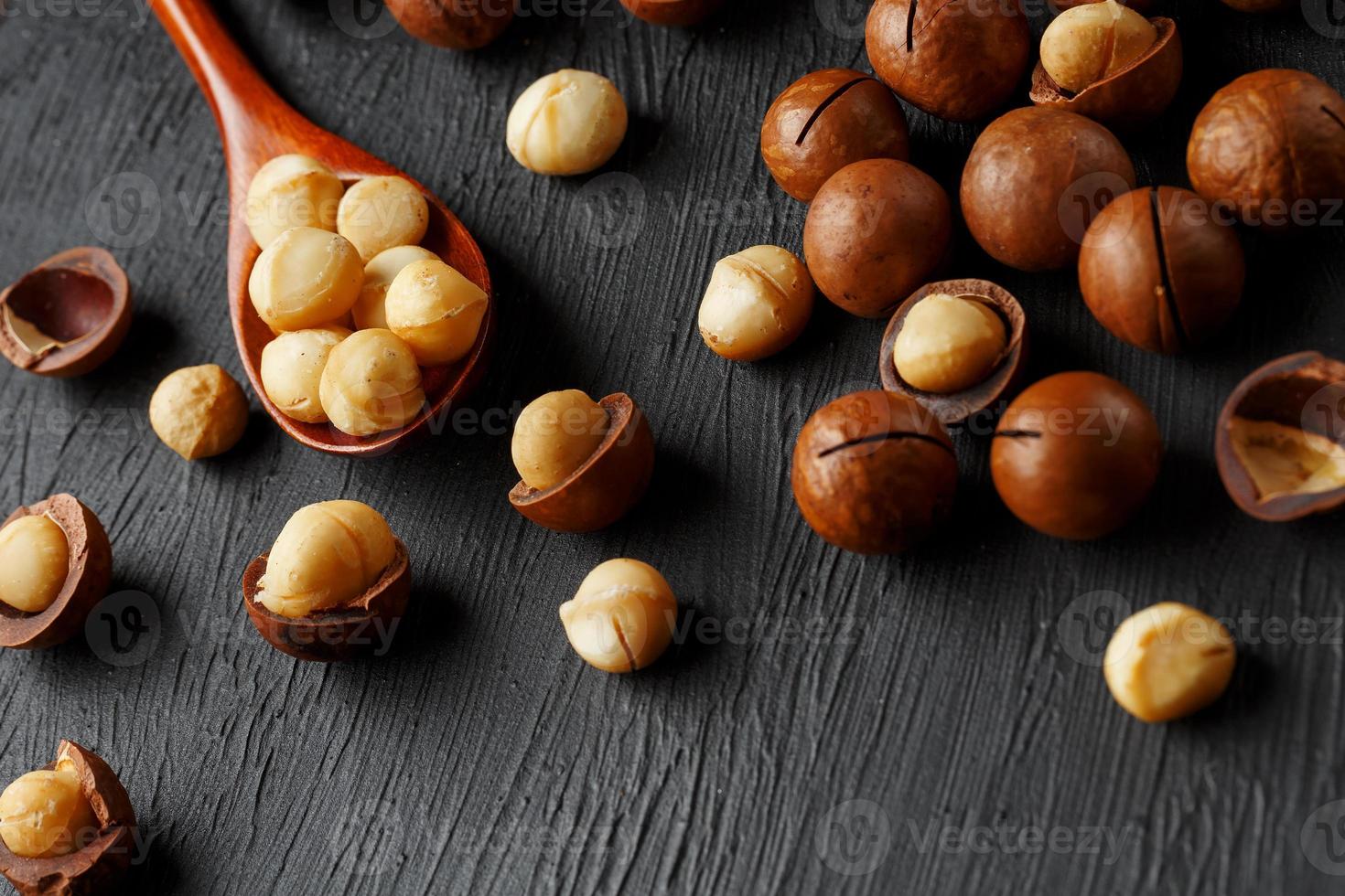 sgusciate macadamia Noce e pelato macadamia Noce su un' nero strutturale sfondo nel un' di legno cucchiaio foto