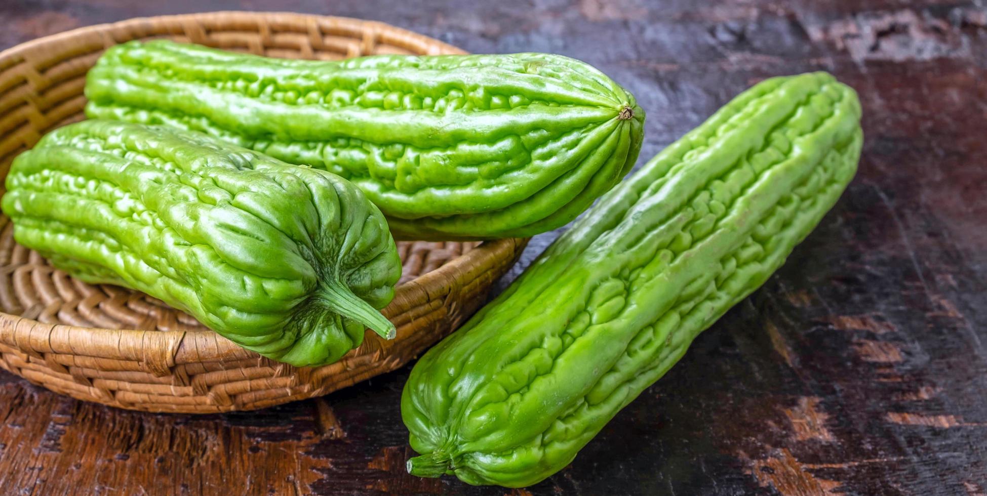 vicino su di fresco verde amaro melone o amaro zucca verdura nel un' cestino posto su un vecchio di legno sfondo foto