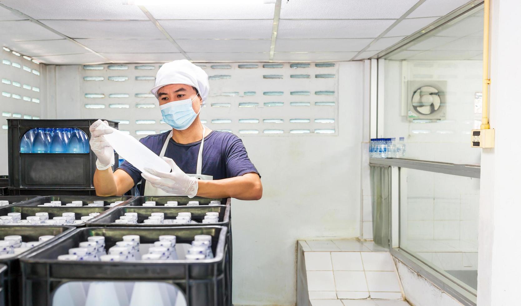 giovane uomo lavoratore o qualità ispettore nel abbigliamento da lavoro e con un' protettivo maschera su il suo viso Lavorando nel controllo in bottiglia potabile acqua nel bevanda acqua fabbrica prima spedizione.bere acqua attività commerciale foto