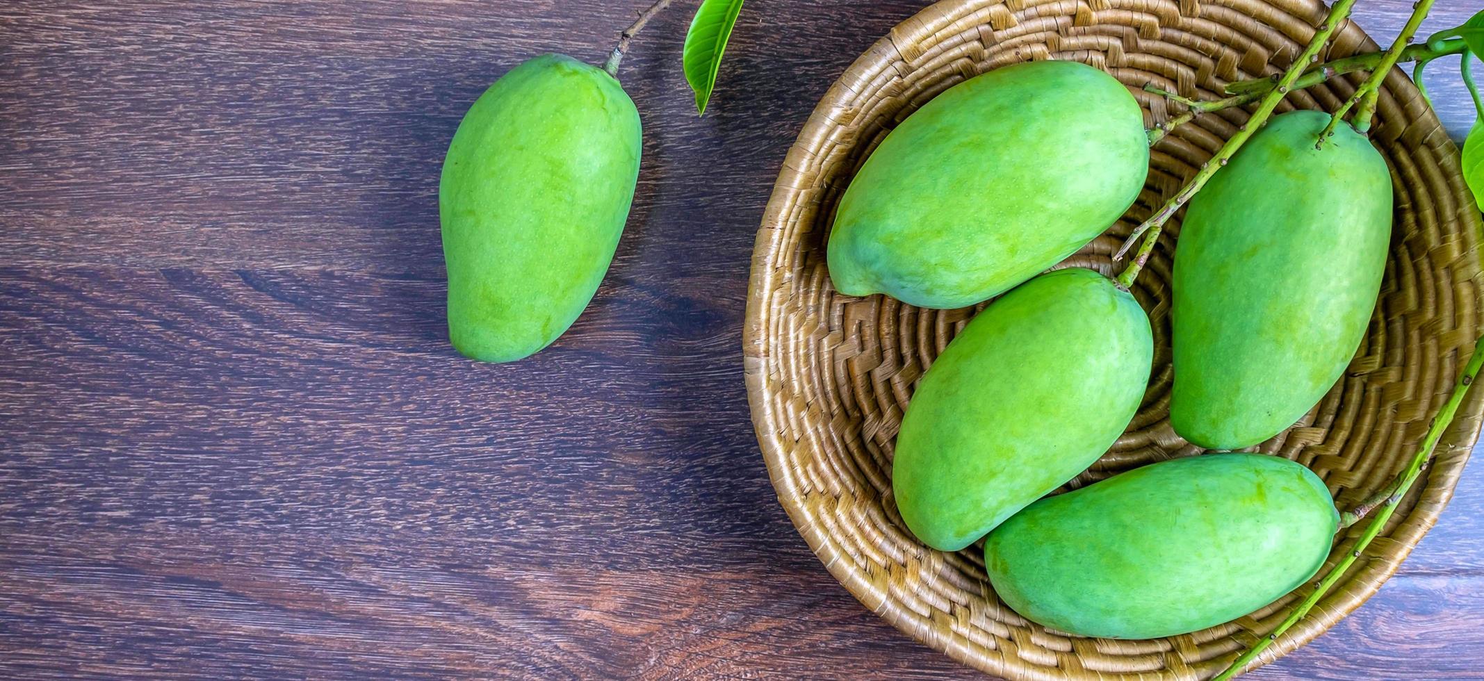 fresco verde Mango e verde foglia nel il cestino ,gruppo di crudo manghi biologico su Marrone di legno sfondov foto