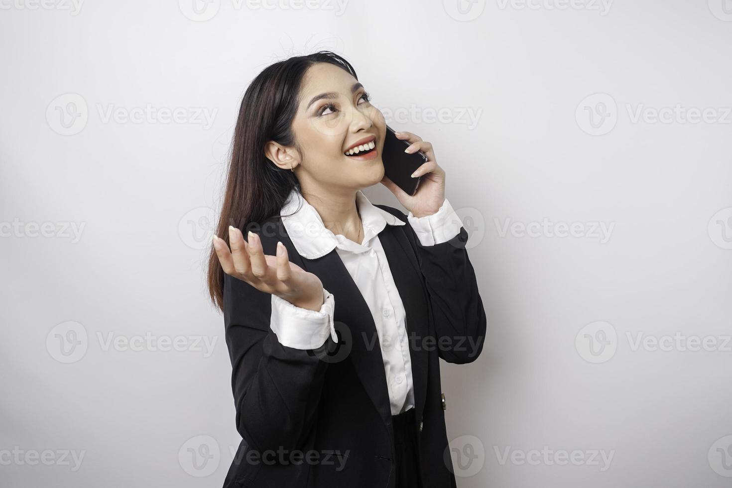 un' ritratto di un' contento asiatico donna d'affari è sorridente mentre parlando su Telefono chiamata indossare un' nero completo da uomo isolato di un' bianca sfondo foto