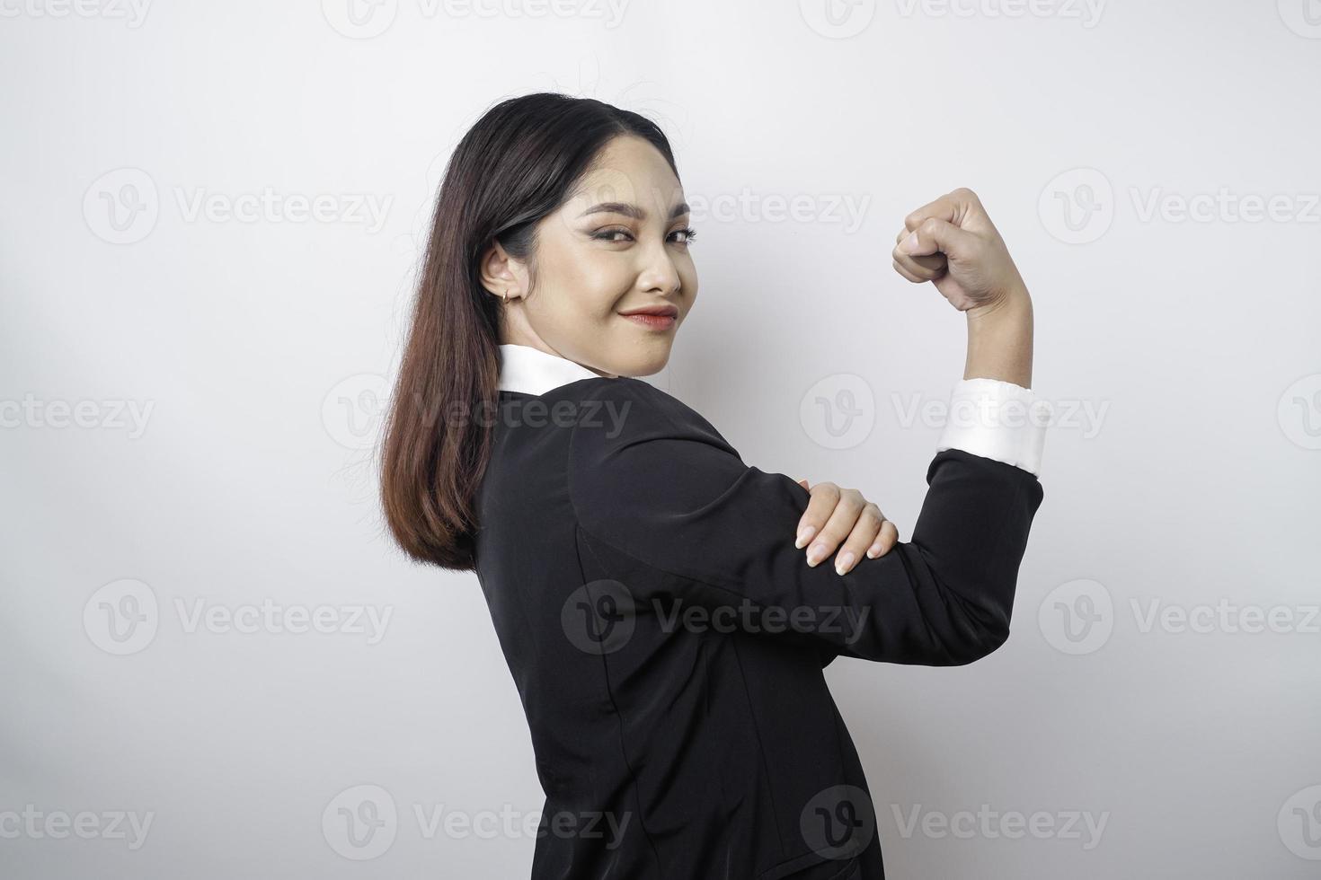 eccitato asiatico attività commerciale donna indossare un' nero completo da uomo mostrando forte gesto di sollevamento sua braccia e muscoli sorridente con orgoglio foto