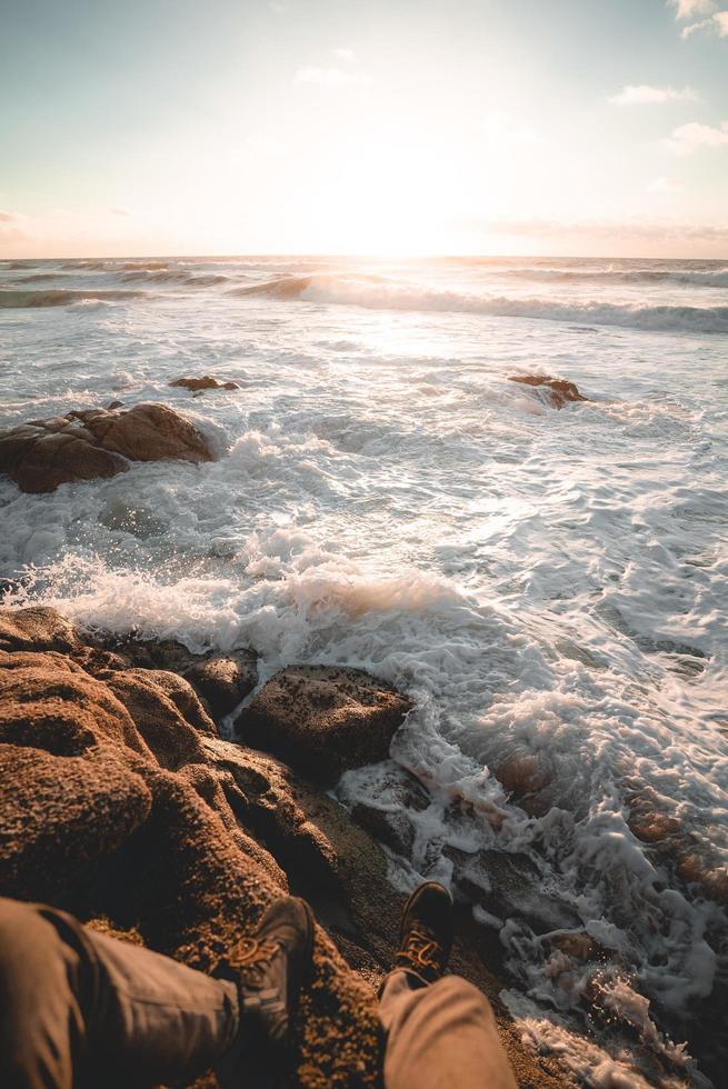 persona seduta sulla roccia accanto alla spiaggia foto