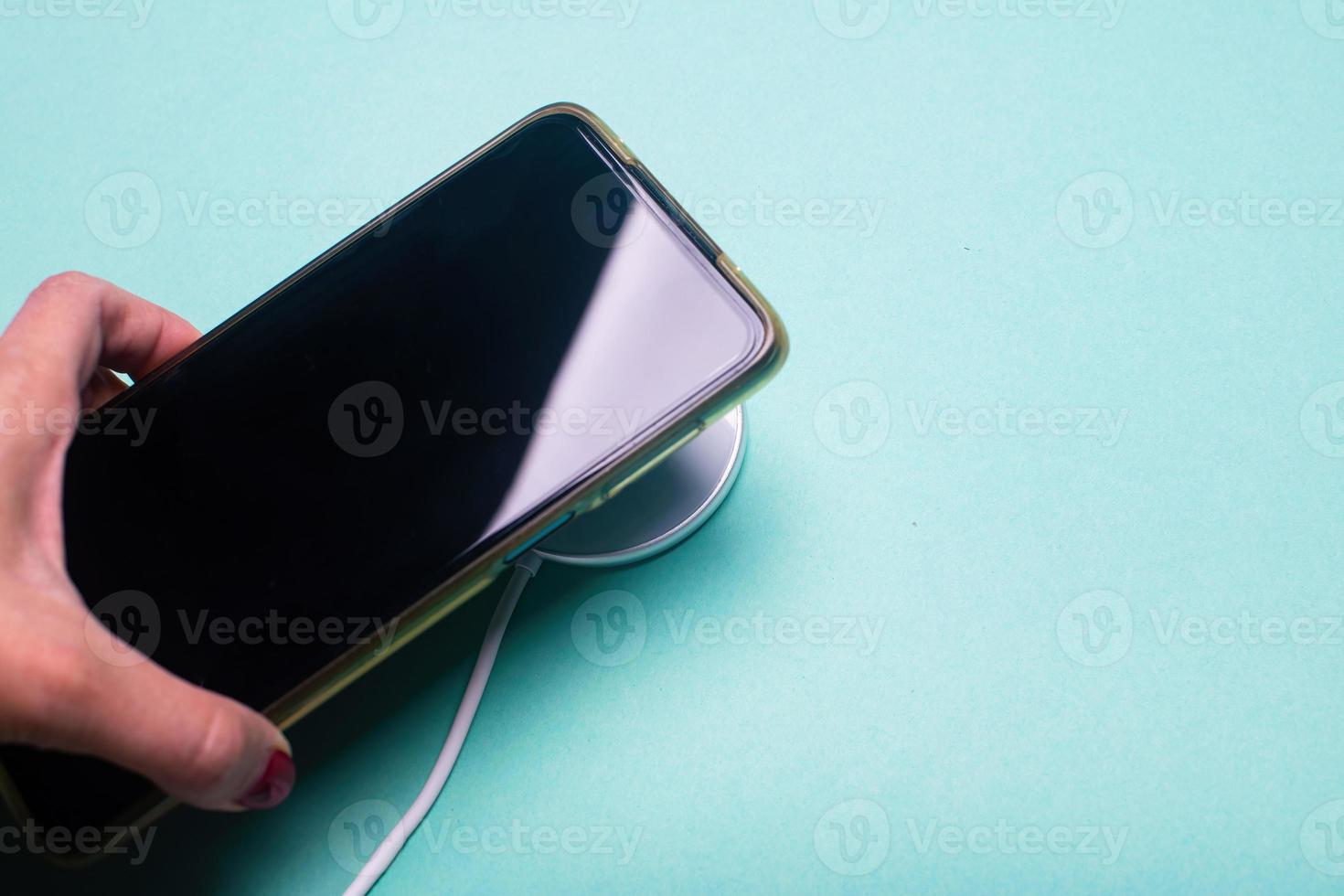donna mano tamponamento un' caricabatterie nel un' smartphone. bianca senza fili ricarica tampone e smartphone su il verde sfondo. foto