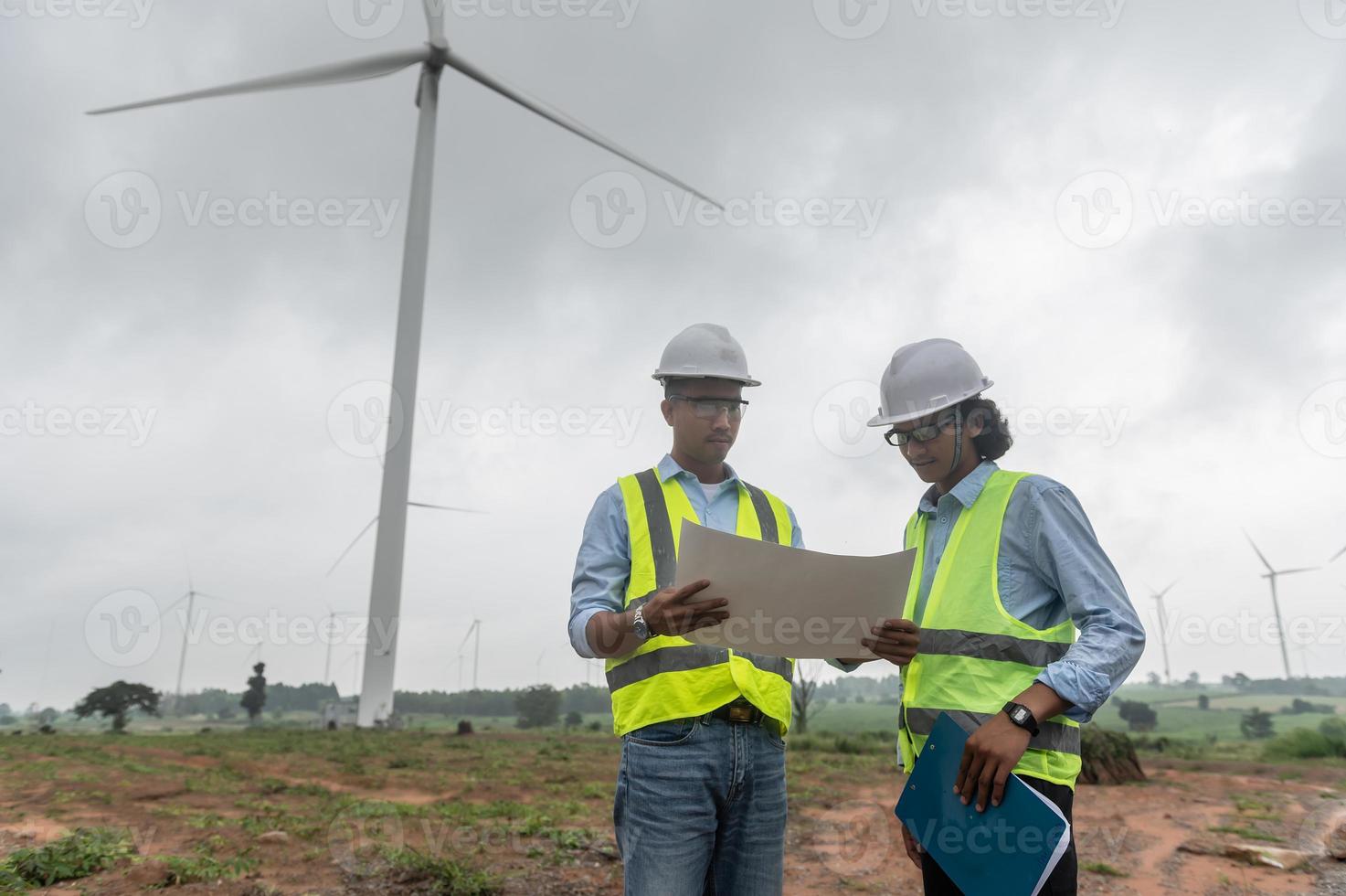 due ingegneri che lavorano e tengono il rapporto alla stazione del generatore di energia dell'azienda agricola della turbina eolica sulla montagna, la gente della Tailandia, l'uomo e la donna del tecnico discutono del lavoro foto