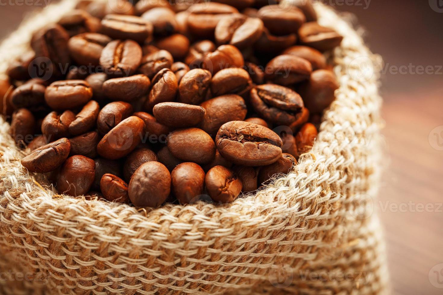 caffè fagioli avvicinamento nel tela ruvida Borsa su di legno sfondo. foto