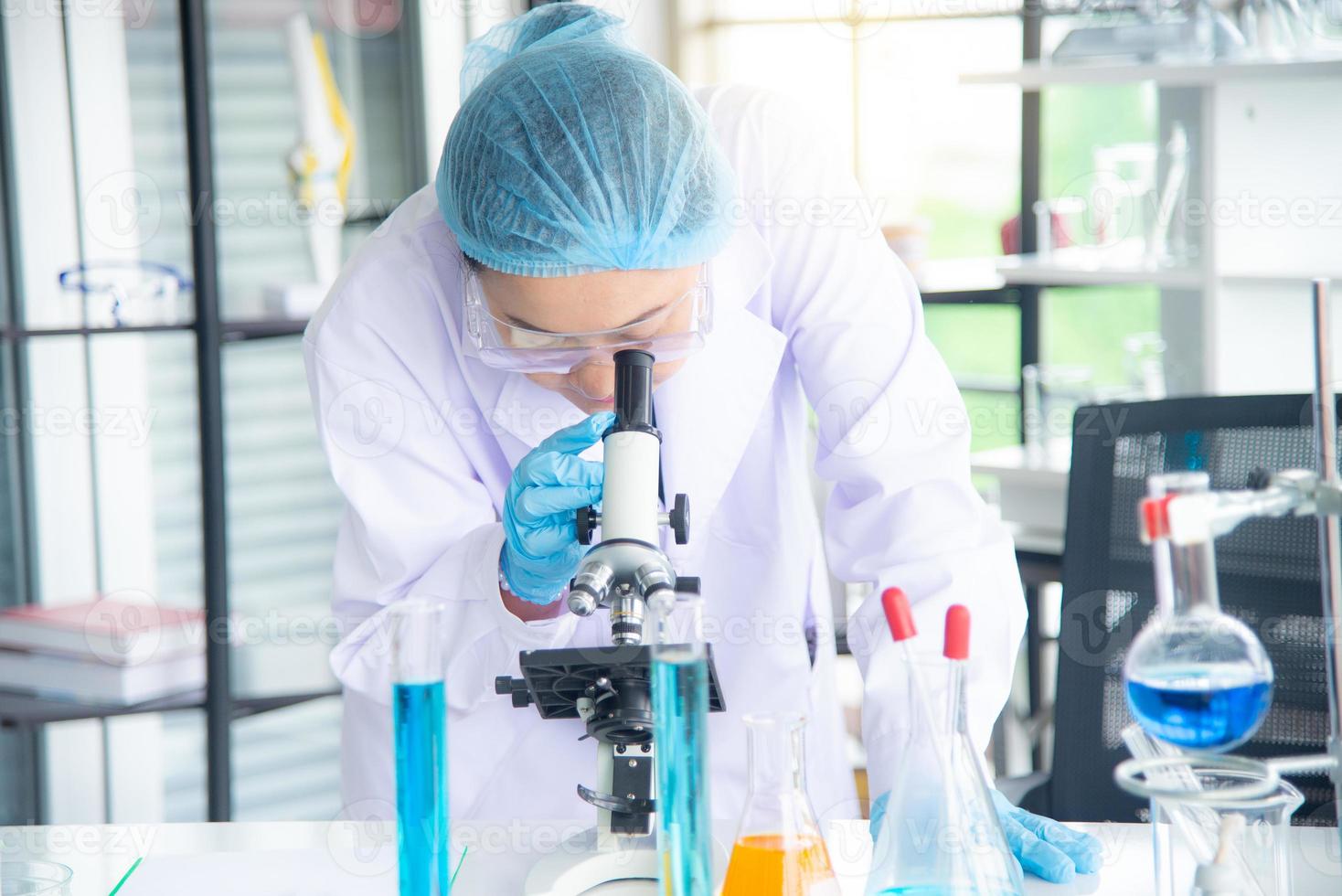 Scienziata, ricercatrice, tecnico o studente asiatica ha condotto ricerche o esperimenti utilizzando il microscopio che è un'attrezzatura scientifica in un laboratorio medico, chimico o biologico foto