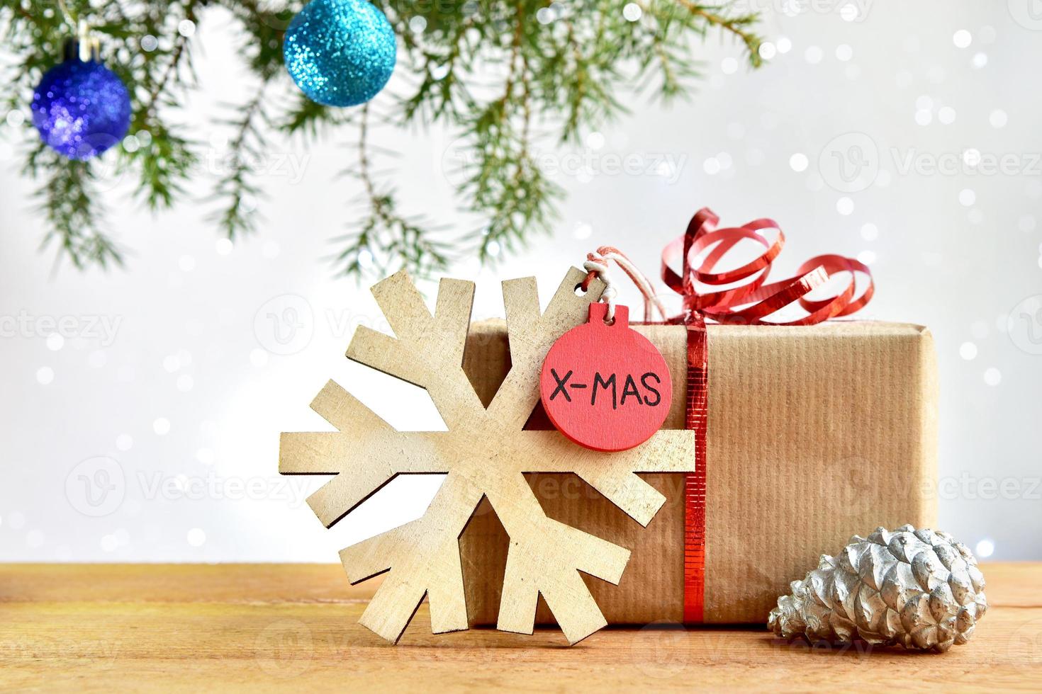 Natale composizione con un' regalo, un' di legno pendente con un' fiocco di neve e un' pino cono su il sfondo di un' Natale albero e bokeh luci. foto