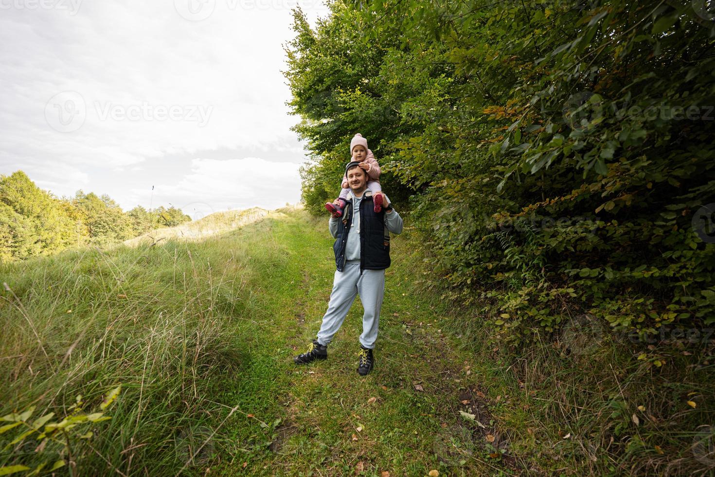 papà con figlia su il suo le spalle a piedi nel foresta. foto