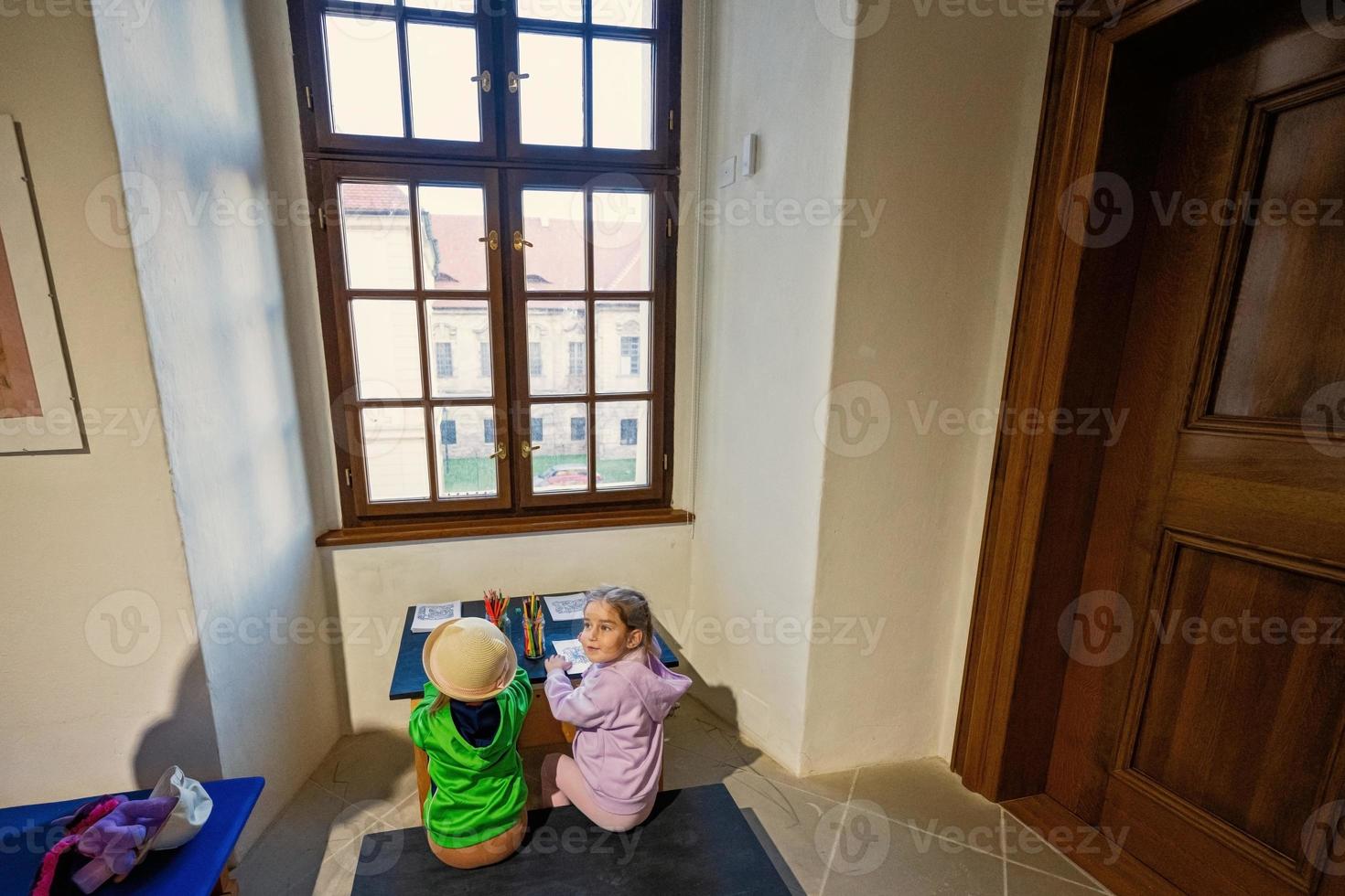 Due sorelle sedersi a il tavolo di fronte finestra e disegno. foto