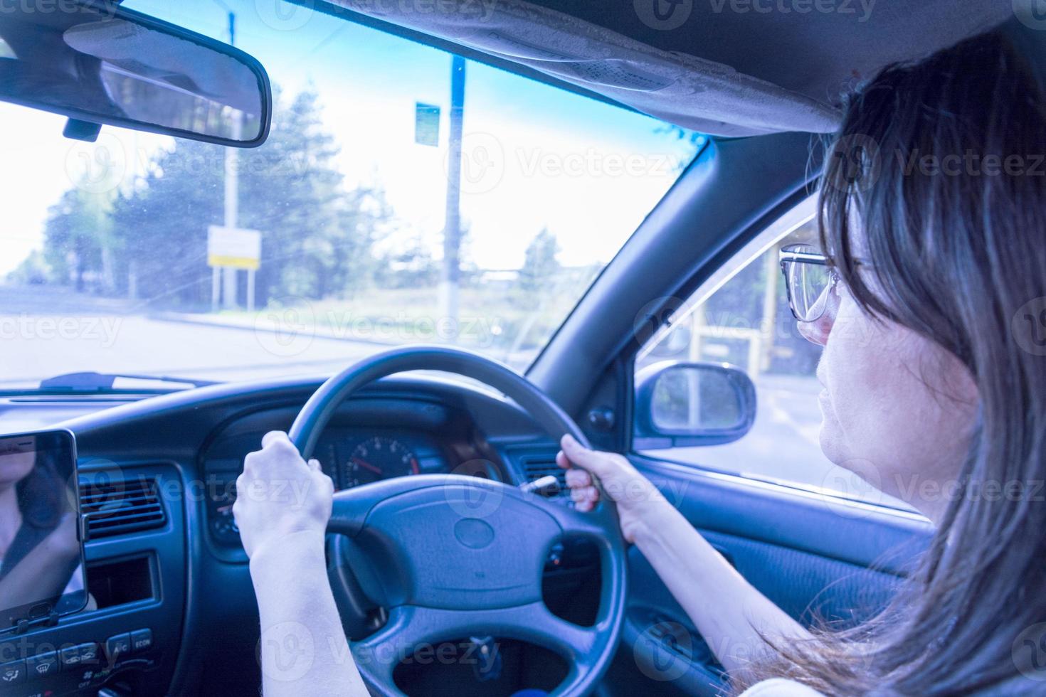 un' brunetta donna con bicchieri è guida un' auto con un' giusto mano guidare foto