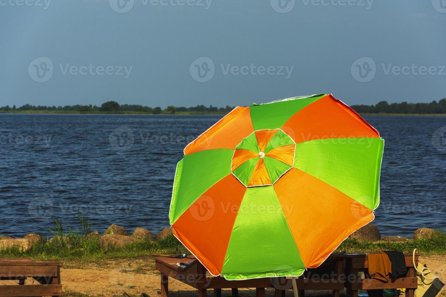 un' spiaggia ombrello a partire dal il sole e un' di legno carrozza longue su il spiaggia, luce del sole, acqua e sabbia. foto