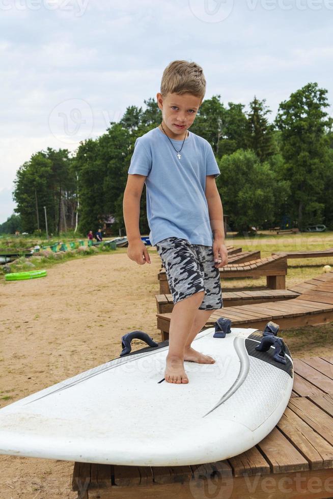 ragazzo imparare per In piedi su il Surf su il spiaggia su il riva di il lago, mare, acqua gli sport, attivo stile di vita, vacanza foto