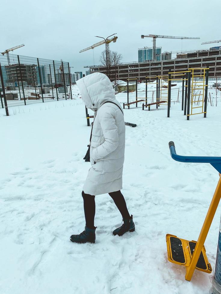 un' ragazza nel un' bianca giù giacca passeggiate nel un' cappuccio nel il neve. inverno nel settentrionale nazione. calore nel caldo Abiti. inverno cose per proteggere il corpo a partire dal temperatura i cambiamenti foto