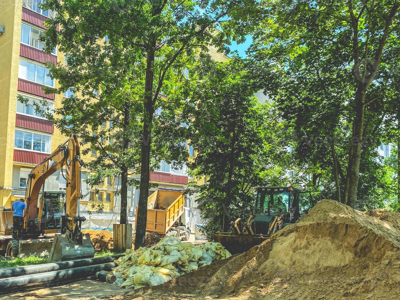 posa comunicazioni nel il cortile. scavatrice scava fori per posa piombatura tubi. posa comunicazioni nel un' Residenziale edificio foto