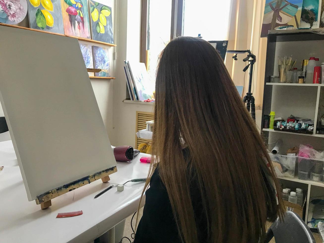 donna artista con lungo capelli disegna un' immagine nel il dell'artista creativo arti laboratorio con vernici e spazzole su il tavolo di il arte scuola foto