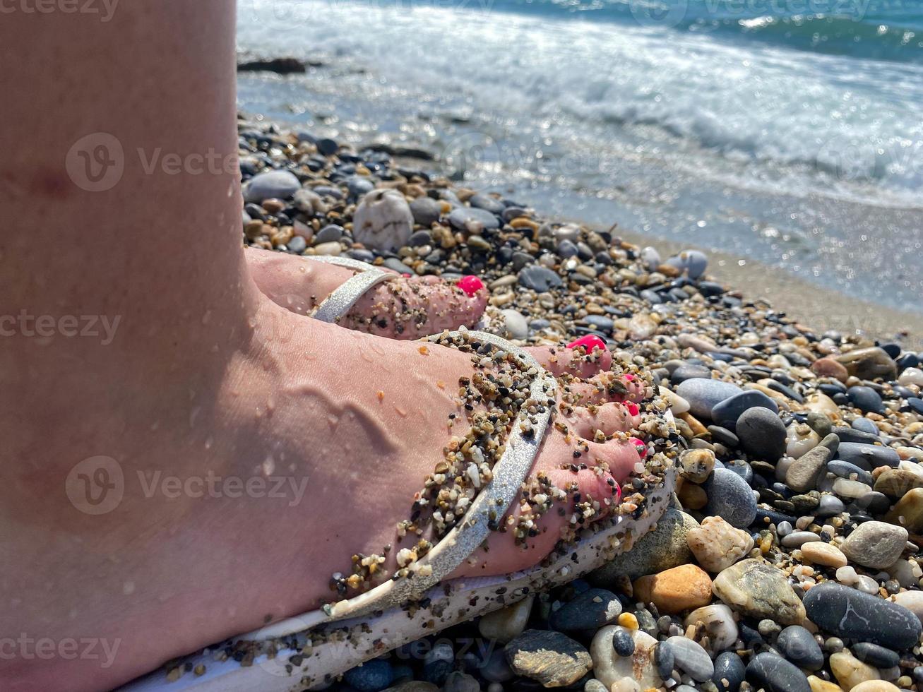 femmina gambe, piedi nel gomma da cancellare pantofole con un' bellissimo rosso pedicure su il sfondo di sabbia su vacanza su il spiaggia nel un' caldo tropicale orientale Paradiso nazione meridionale ricorrere foto