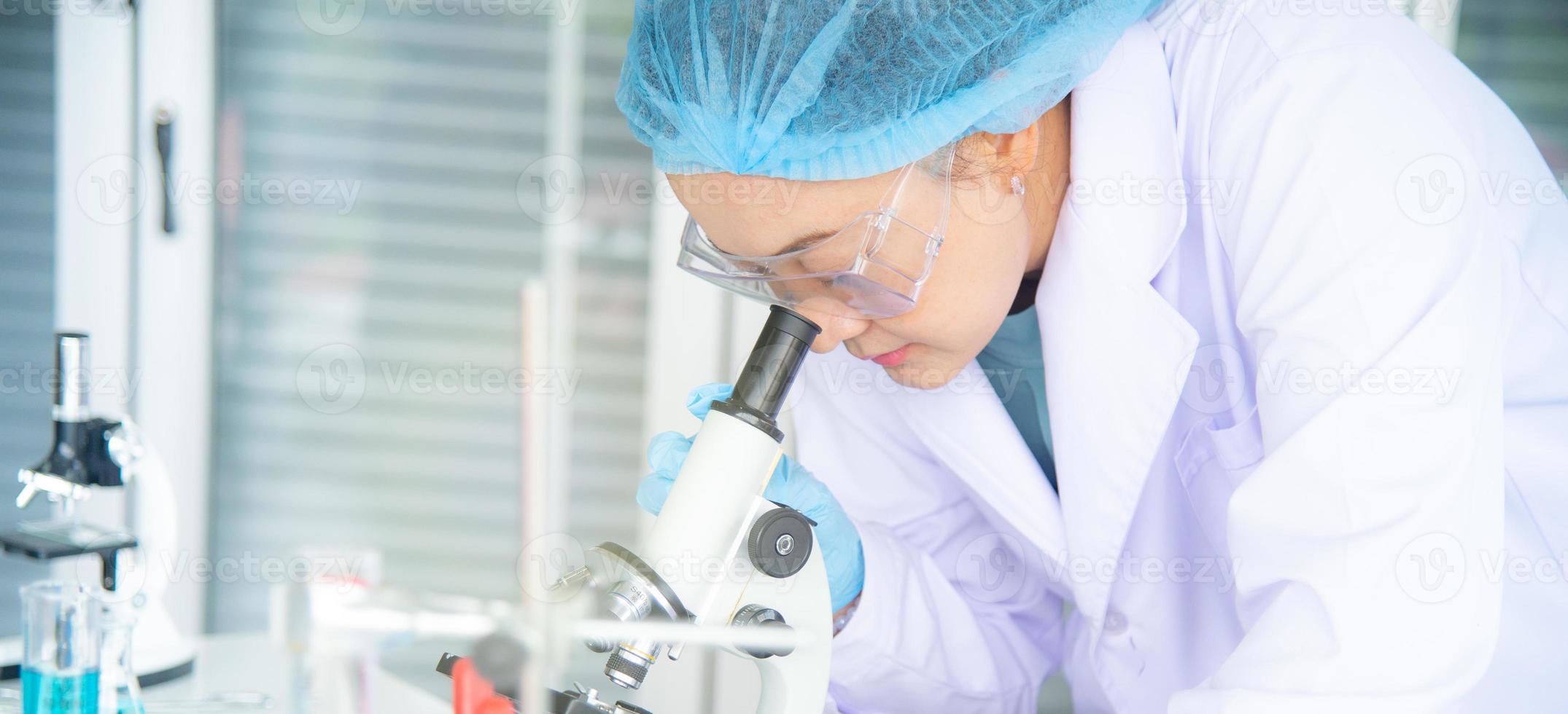 Scienziata, ricercatrice, tecnico o studente asiatica ha condotto ricerche o esperimenti utilizzando il microscopio che è un'attrezzatura scientifica in un laboratorio medico, chimico o biologico foto