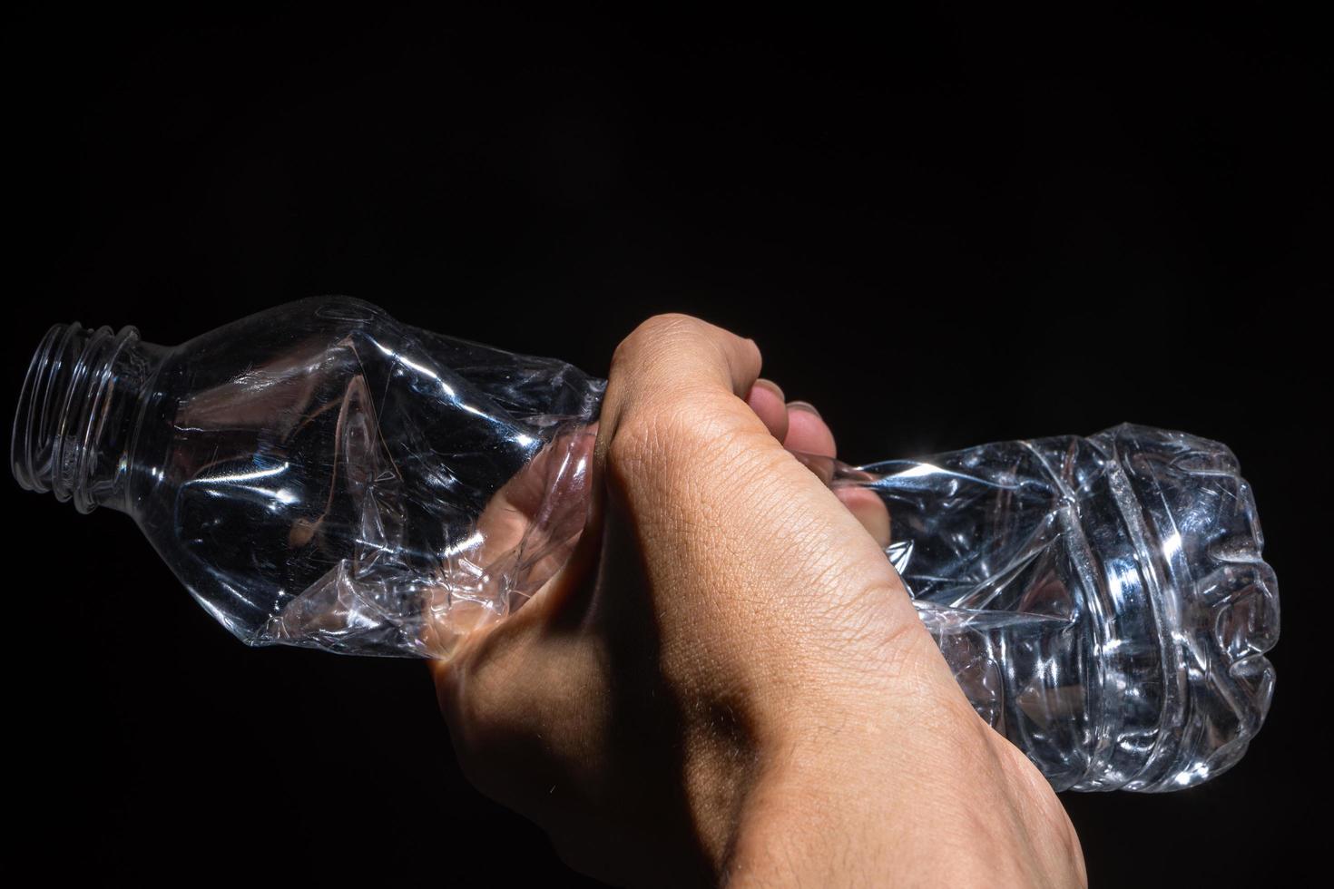 mano che tiene una bottiglia di plastica su sfondo nero foto