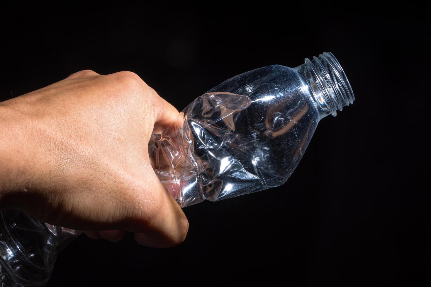 mano che tiene una bottiglia di plastica su sfondo nero foto