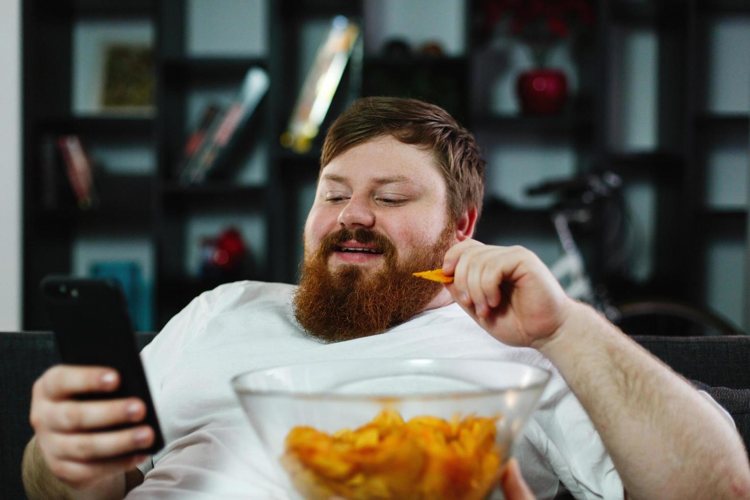 uomo che mangia patatine mentre controlla il suo telefono foto