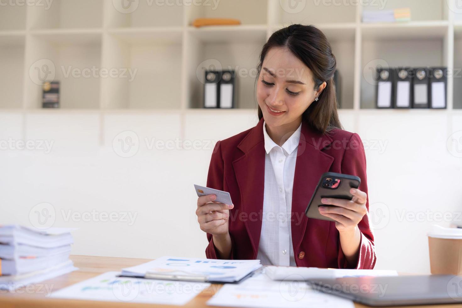 contento asiatico attività commerciale donna pagare in linea utilizzando mobile Telefono a il ufficio. foto