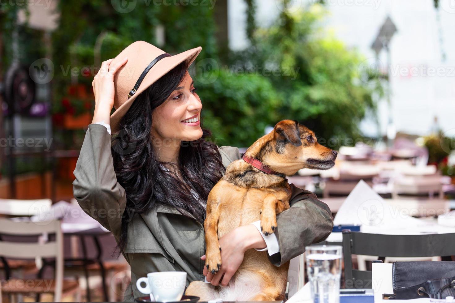 attraente giovane donna seduta nel caffè negozio, rilassante e Tenere sua cane. animale domestico amichevole caffetteria, bellissimo ragazza con sua cane ubicazione a un' caffè negozio e bevanda caffè. foto