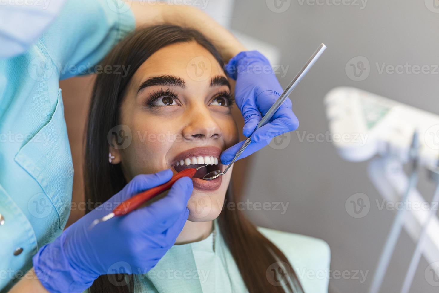 sorridente brunetta donna essere esaminato di dentista a dentale clinica. mani di un' medico Tenere dentale strumenti vicino del paziente bocca. salutare denti e medicina concetto foto