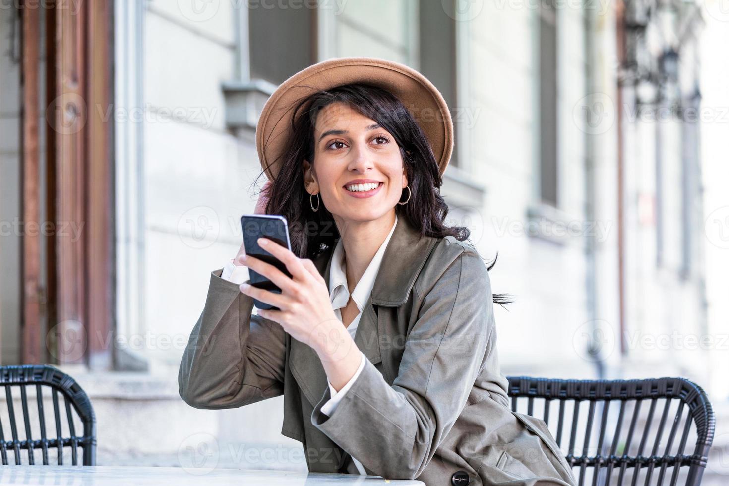 giovane bellissimo donna guardare a smartphone mentre seduta a caffetteria. contento Università alunno utilizzando mobile Telefono. donna d'affari potabile caffè, sorridente e utilizzando smartphone interno. foto