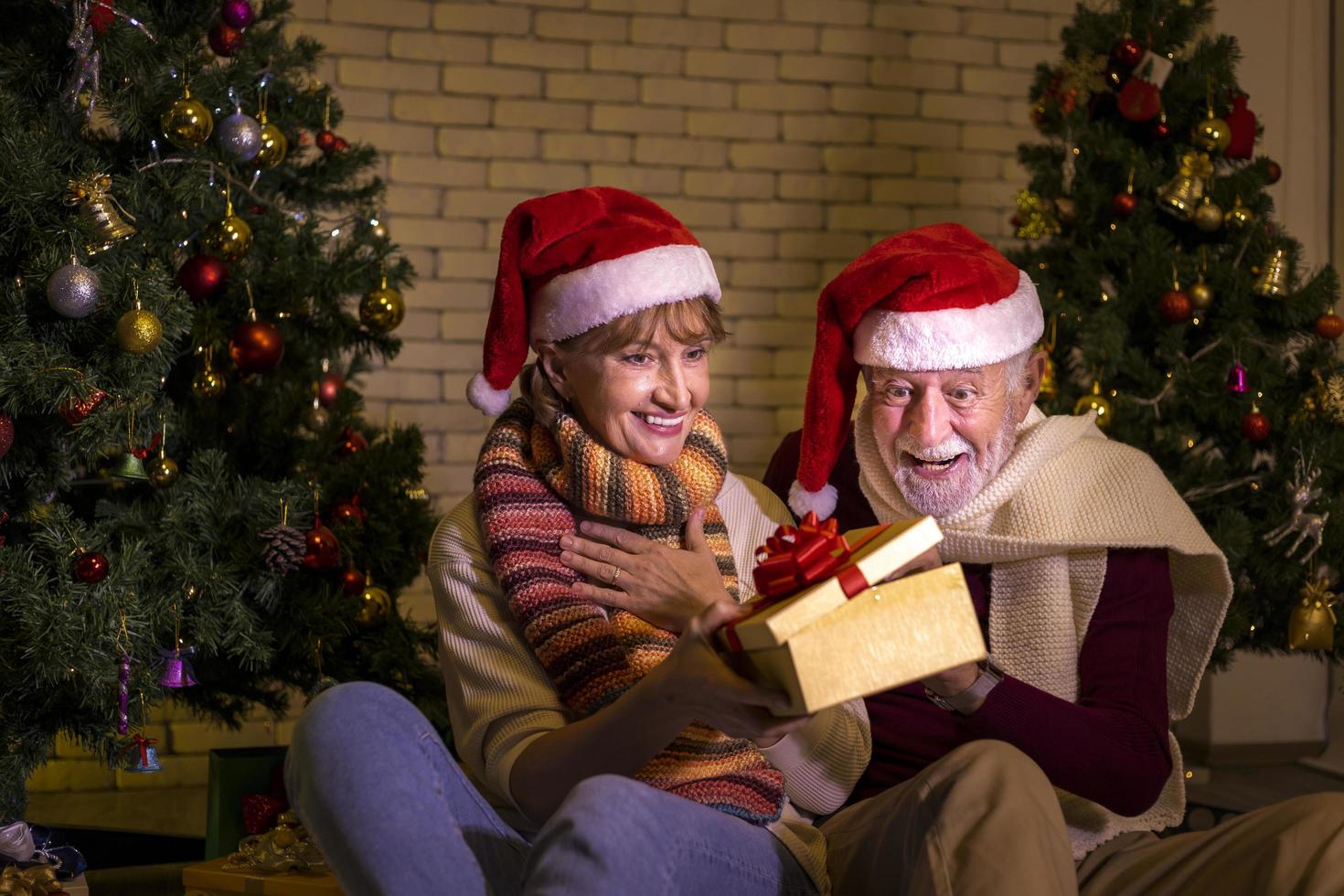 anziano caucasico coppia festeggiare Natale insieme nel felicità e eccitazione a casa con Santa cappello e Natale albero foto