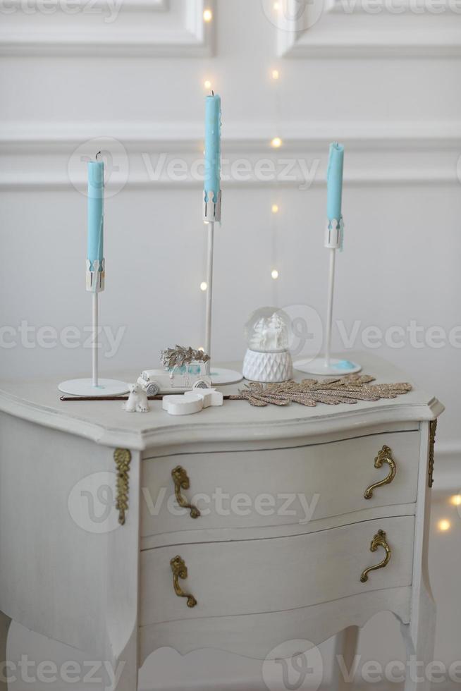 bianca legna capezzale tavolo, il petto di cassetti nel il Camera da letto. candele su il capezzale tavolo interno. mobilia serie. moderno design foto
