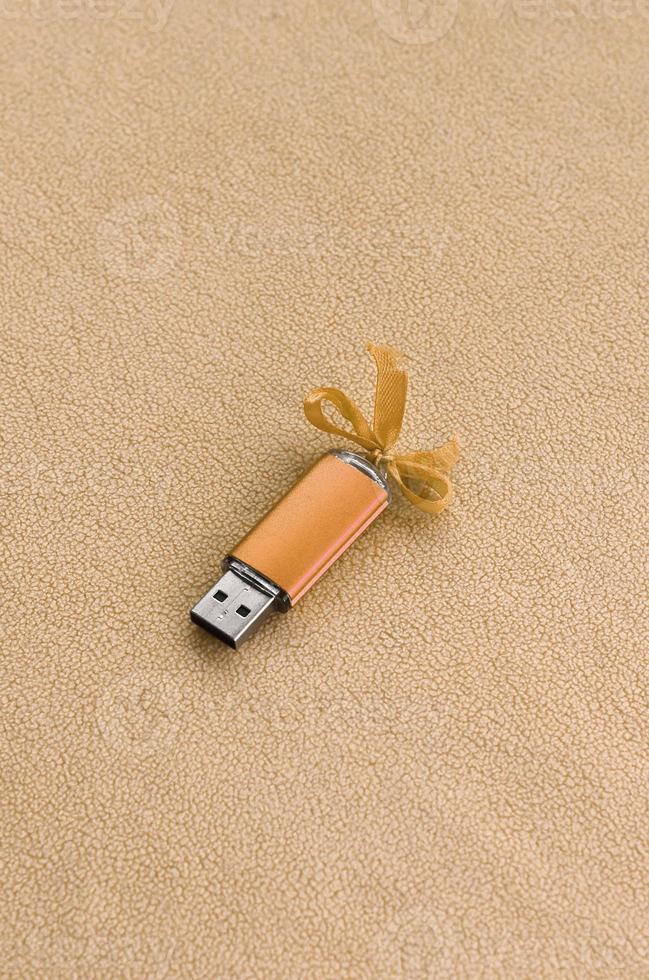 arancia USB veloce memoria carta con un' blu arco bugie su un' coperta di morbido e peloso leggero arancia vello tessuto. classico femmina regalo design per un' memoria carta foto