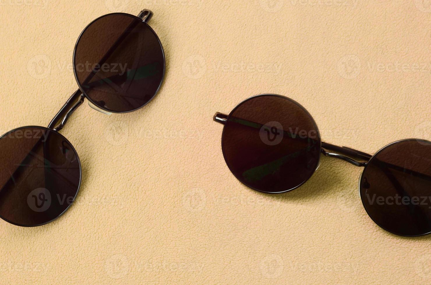 Due elegante nero occhiali da sole con il giro bicchieri bugie su un' coperta fatto di morbido e soffice leggero arancia vello tessuto. alla moda sfondo immagine nel moda colori foto