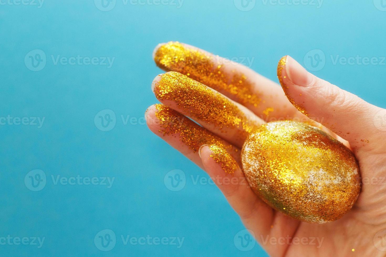Pasqua d'oro uovo nel il mano su un' blu sfondo. Pasqua sfondo. mano e uovo nel oro brilla. contento Pasqua foto