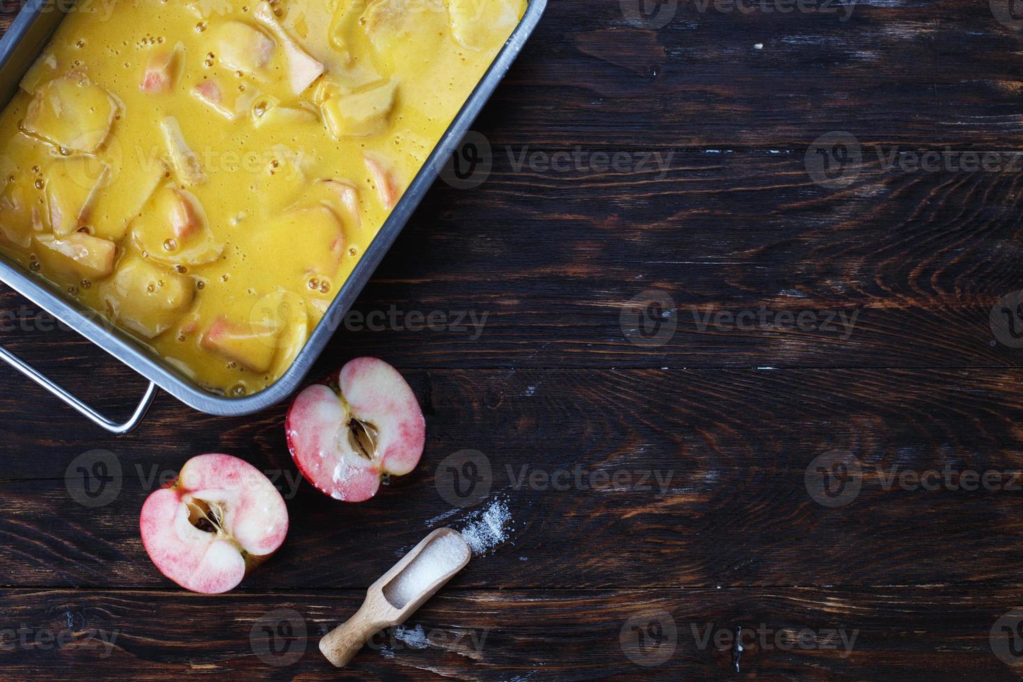 fabbricazione un Mela torta. crudo Impasto nel un' cottura al forno piatto, Mela e zucchero su il di legno tavolo foto