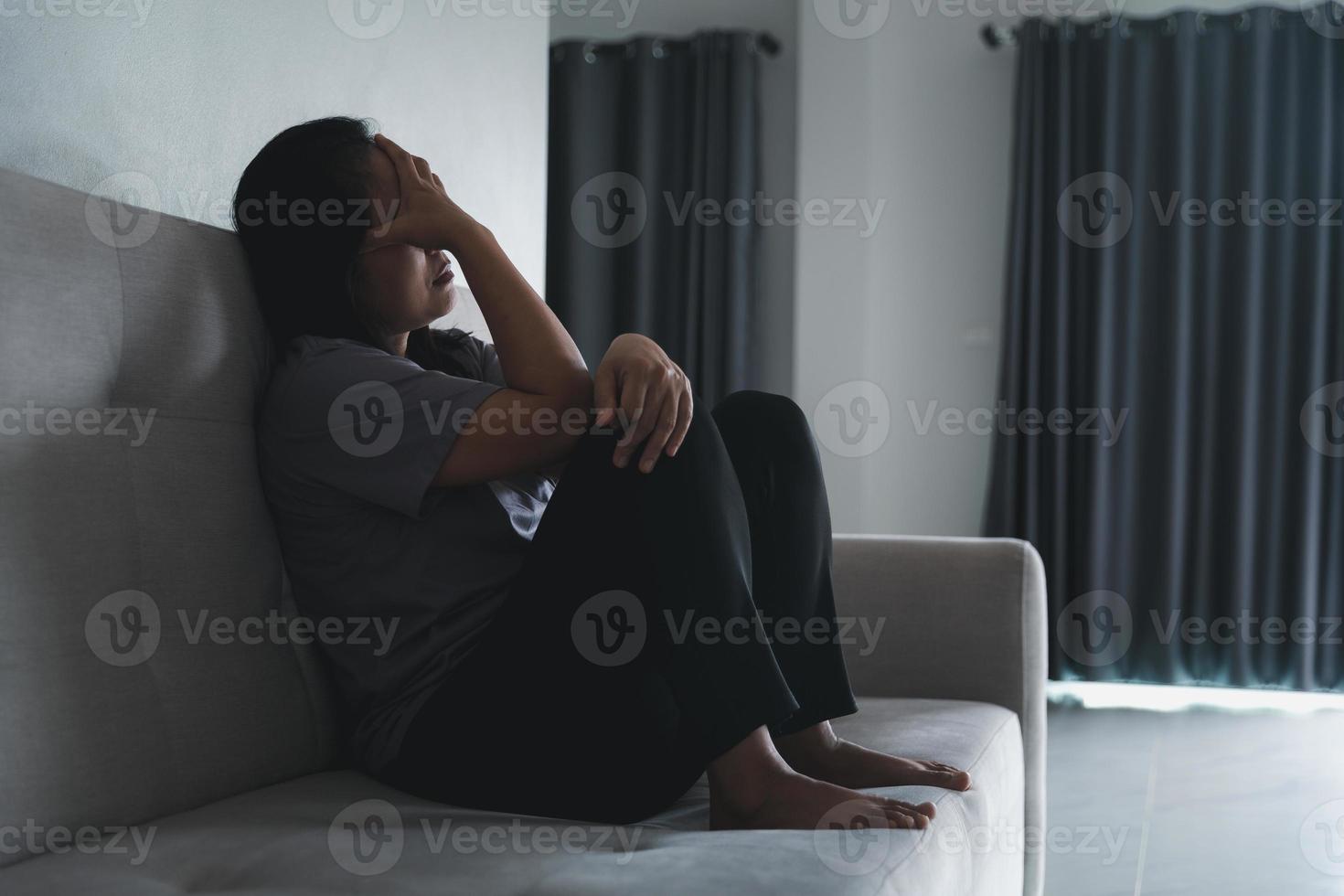 schizofrenia con solitario e triste nel mentale Salute depressione concetto. depresso donna seduta contro su il divano a casa con buio camera sensazione miserabile. donne siamo depresso, pauroso e infelice. foto