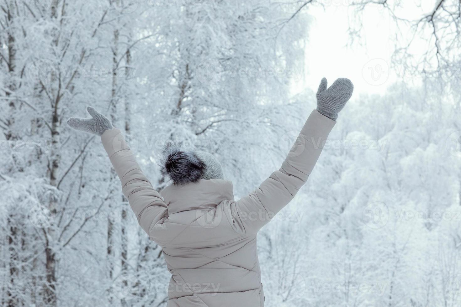 contento donna nel a maglia grigio cappello con pompon a partire dal dietro a di inverno foresta nevicando foto