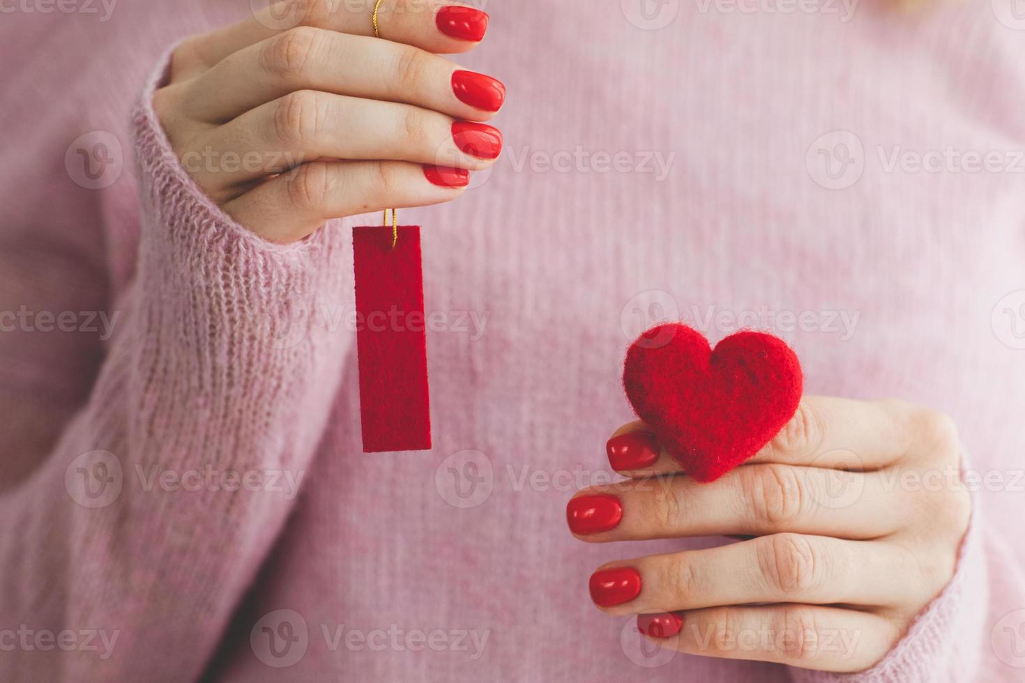 vicino su donna di mani con rosso manicure detiene cuore sotto lana pastello rosa a maglia maglione sfondo io amore voi simbolo San Valentino giorno foto