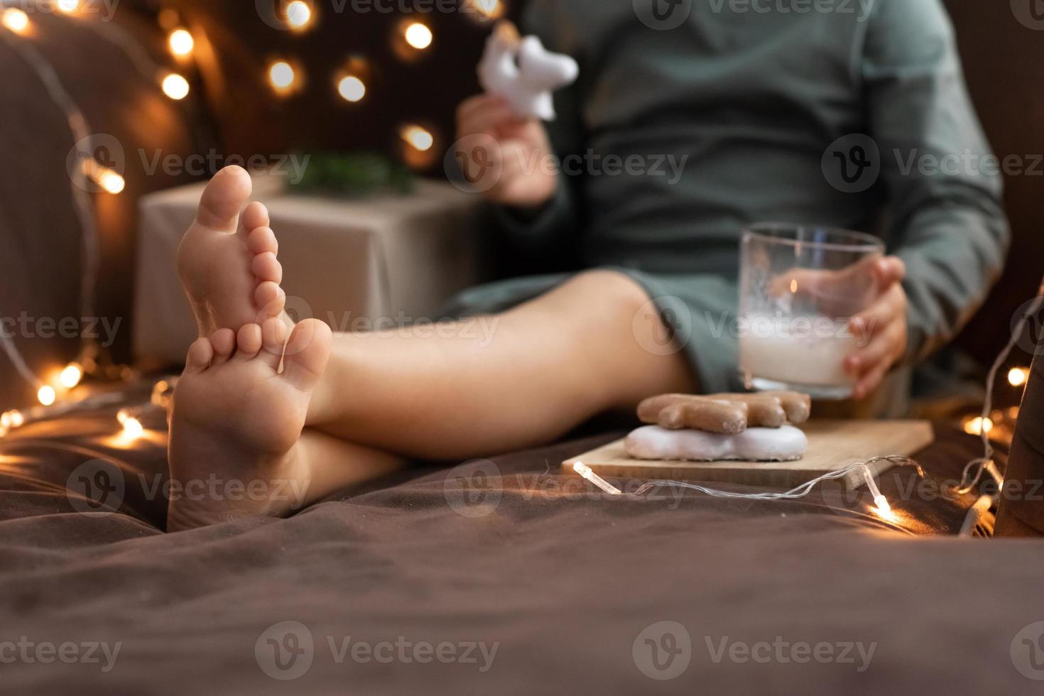 vicino su bambino spoglio piedi, bicchiere di latte cannella zabaione, natale dolci Zenzero biscotti, artigianato carta scatola regalo. ragazzo Natale mattina prima colazione. zabaione foto