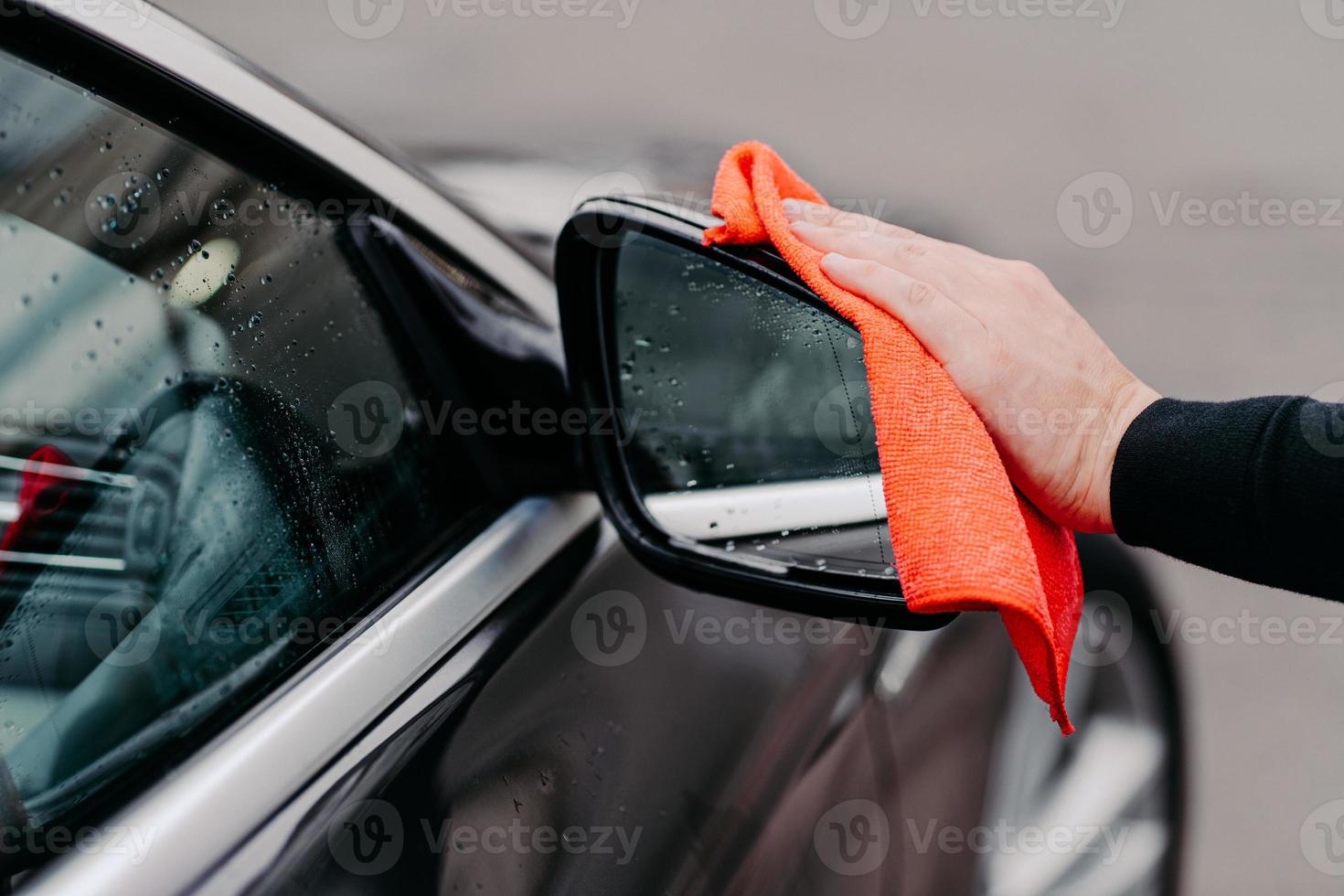 primo piano della mano dell'uomo che pulisce l'acqua sull'auto nera con un panno in microfibra. concentrarsi sullo specchietto laterale automatico. trasporto self service foto