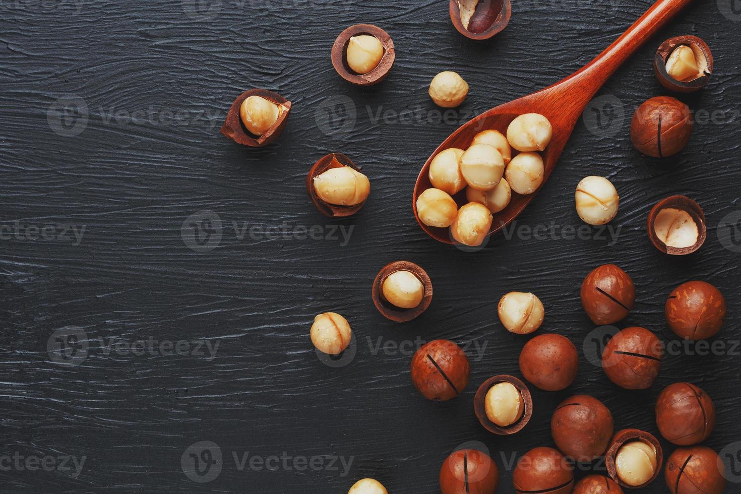 sgusciate macadamia Noce e pelato macadamia Noce su un' nero strutturale sfondo nel un' di legno cucchiaio. Basso contrasto foto