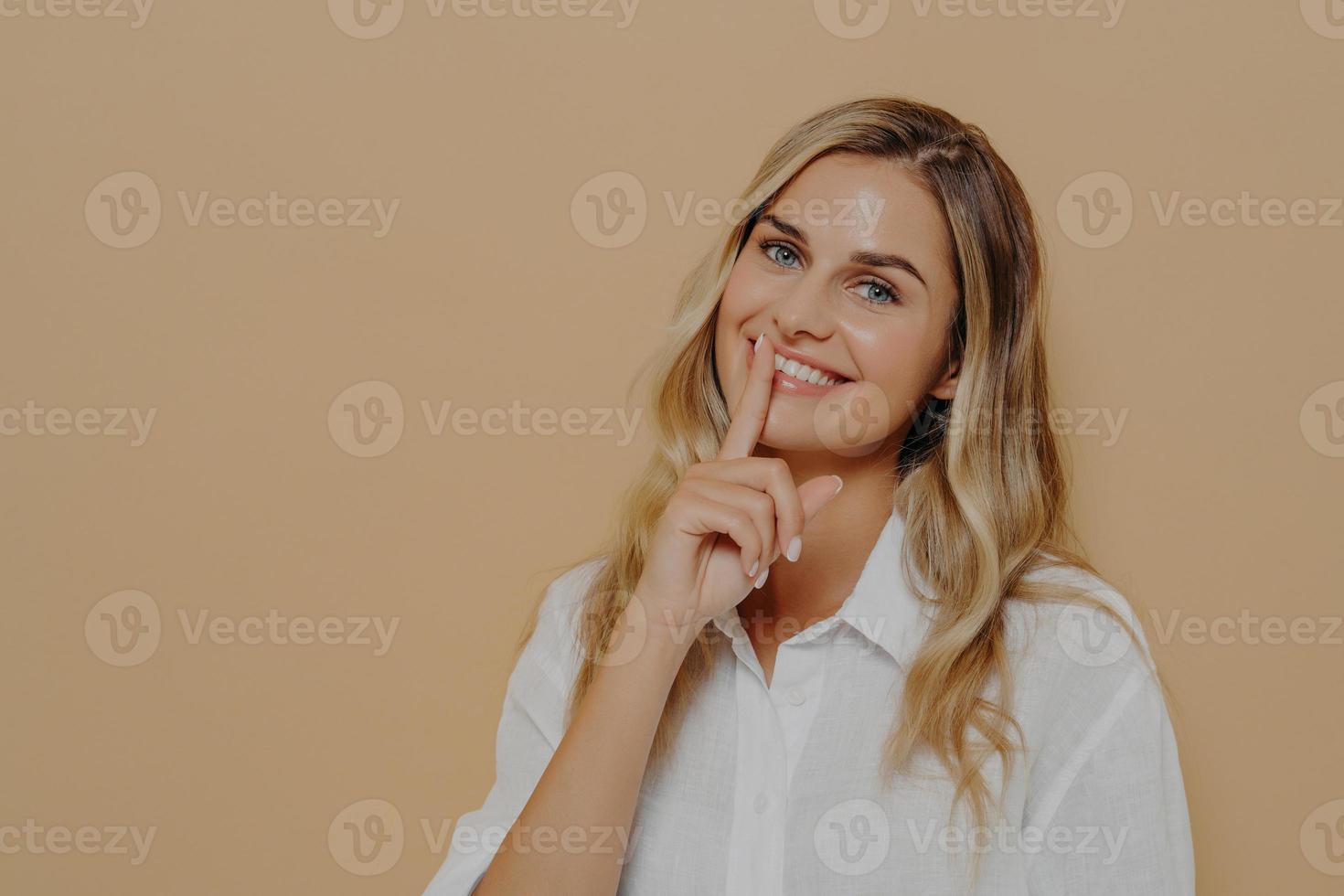 bella giovane donna con lunghi capelli biondi tinti mostra il segno del silenzio o mantiene il gesto del silenzio foto