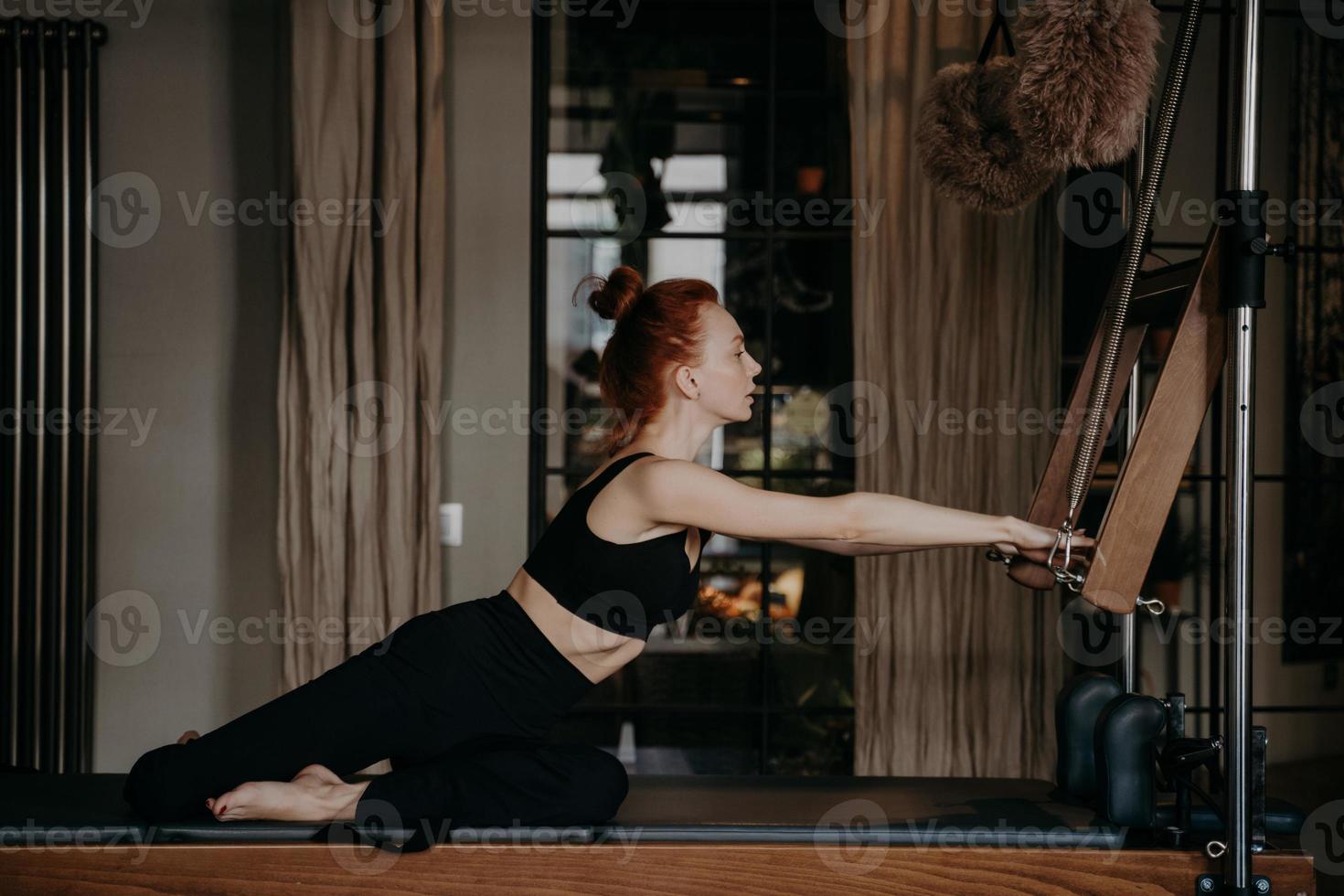 donna sportiva zenzero che allunga il corpo atletico su cadillac reformer durante l'allenamento pilates foto