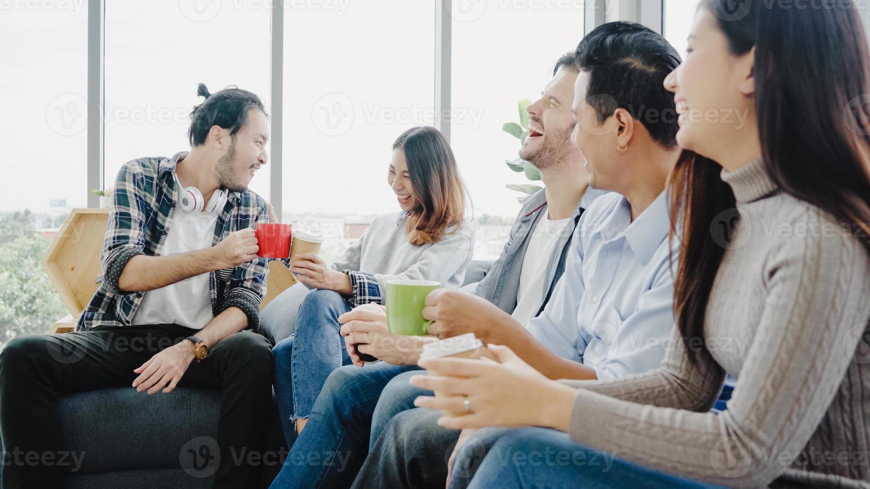 diversità di giovani gruppo squadra in possesso di tazze di caffè e discutere di qualcosa con un sorriso mentre era seduto sul divano in ufficio. pausa caffè presso l'ufficio creativo. foto