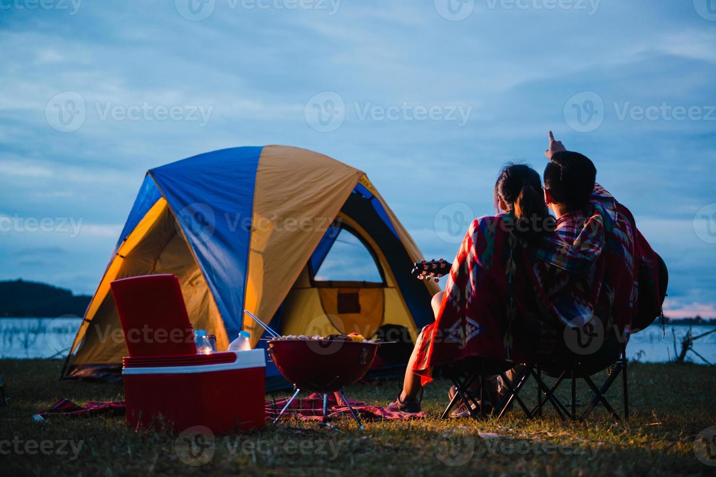 tenda spensierato coppia rilassante a distanza viaggio concetto - romantico asiatico coppia turisti seduta a un' fuoco di bivacco vicino tenda, abbracciare ogni altro sotto alberi e notte cielo. notte campeggio foto