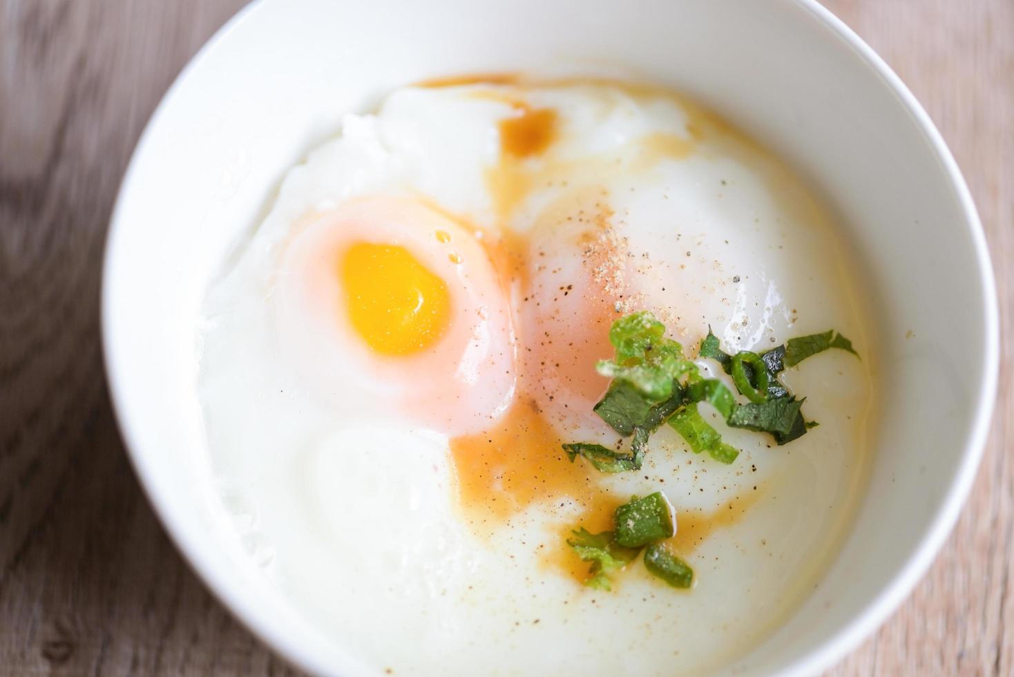 bollito uova su bianca ciotola con Pepe coriandolo su di legno tavolo, uovo colazione, onsen uovo foto