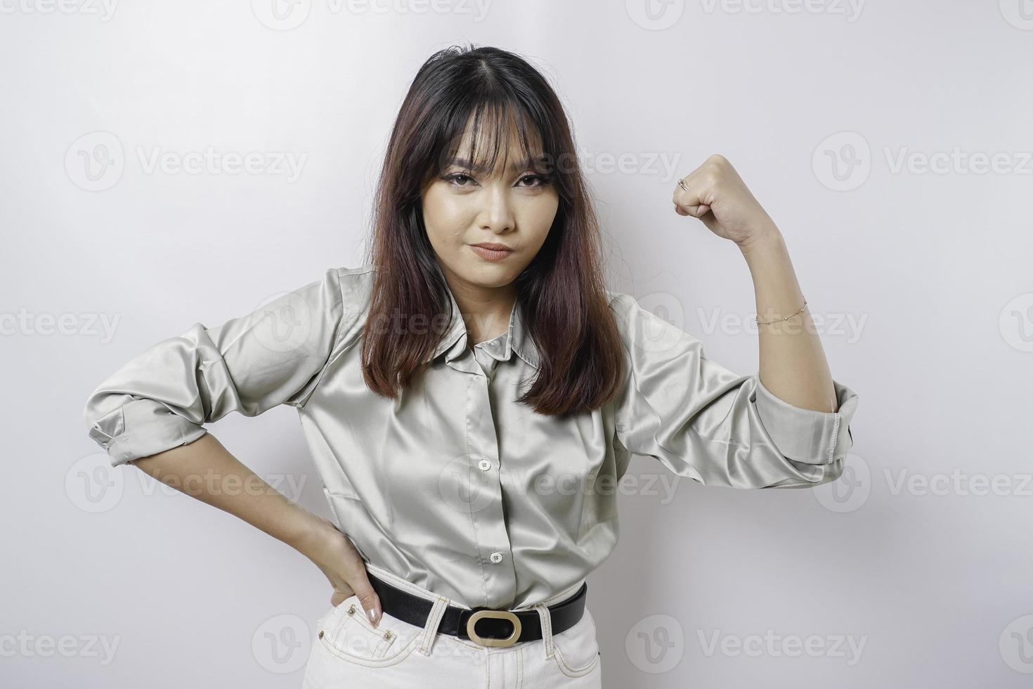 eccitato asiatico donna indossare un' saggio verde camicia mostrando forte gesto di sollevamento sua braccia e muscoli sorridente con orgoglio foto
