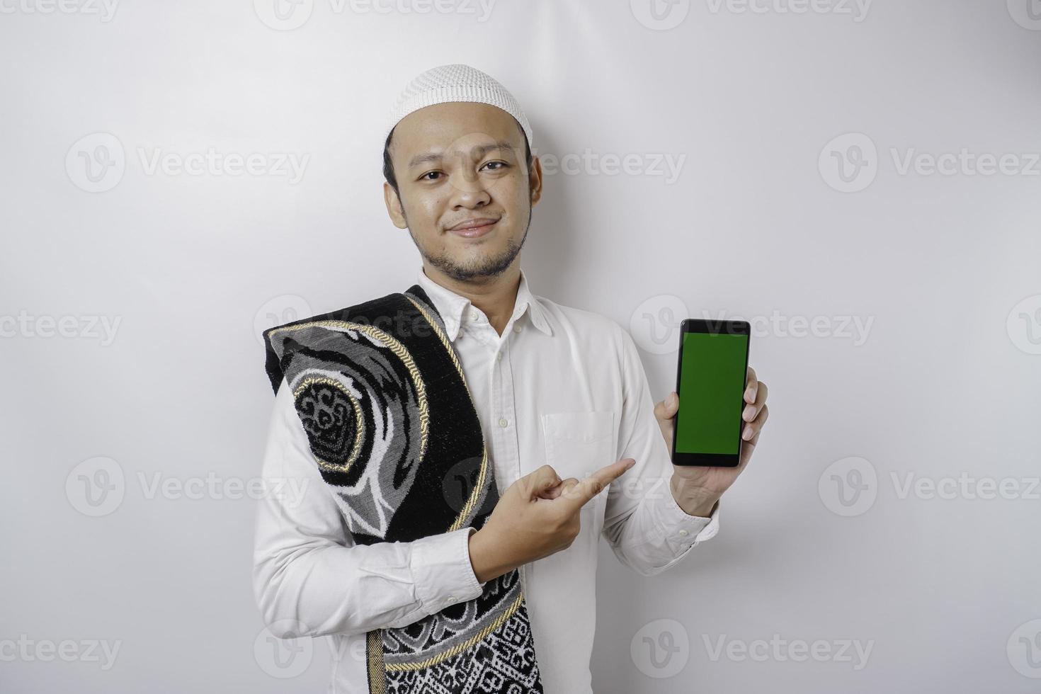 un' ritratto di un' contento asiatico musulmano uomo sorridente mentre mostrando copia spazio su il suo Telefono, isolato di bianca sfondo foto